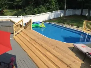 Pressure-treated wood pool deck in Enfield, CT, featuring wide steps, wooden railings, and seamless access to an above-ground pool for lounging and relaxation.